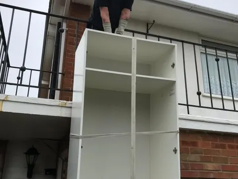 Reliable Removals mover lifting a tall cabinet over a balcony rail