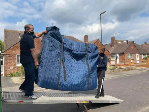 Reliable Removals crew carrying a wrapped armchair down the van ramp