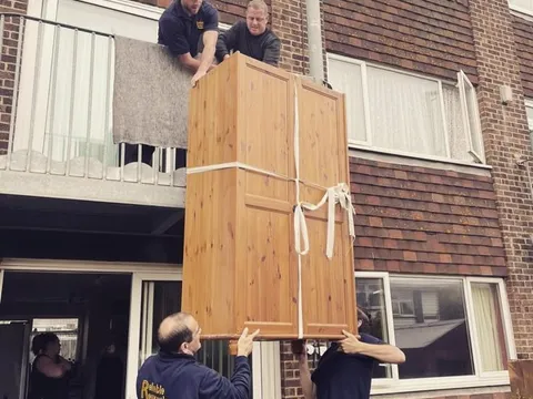 Reliable Removals crew lowering a pine wardrobe from a first floor balcony